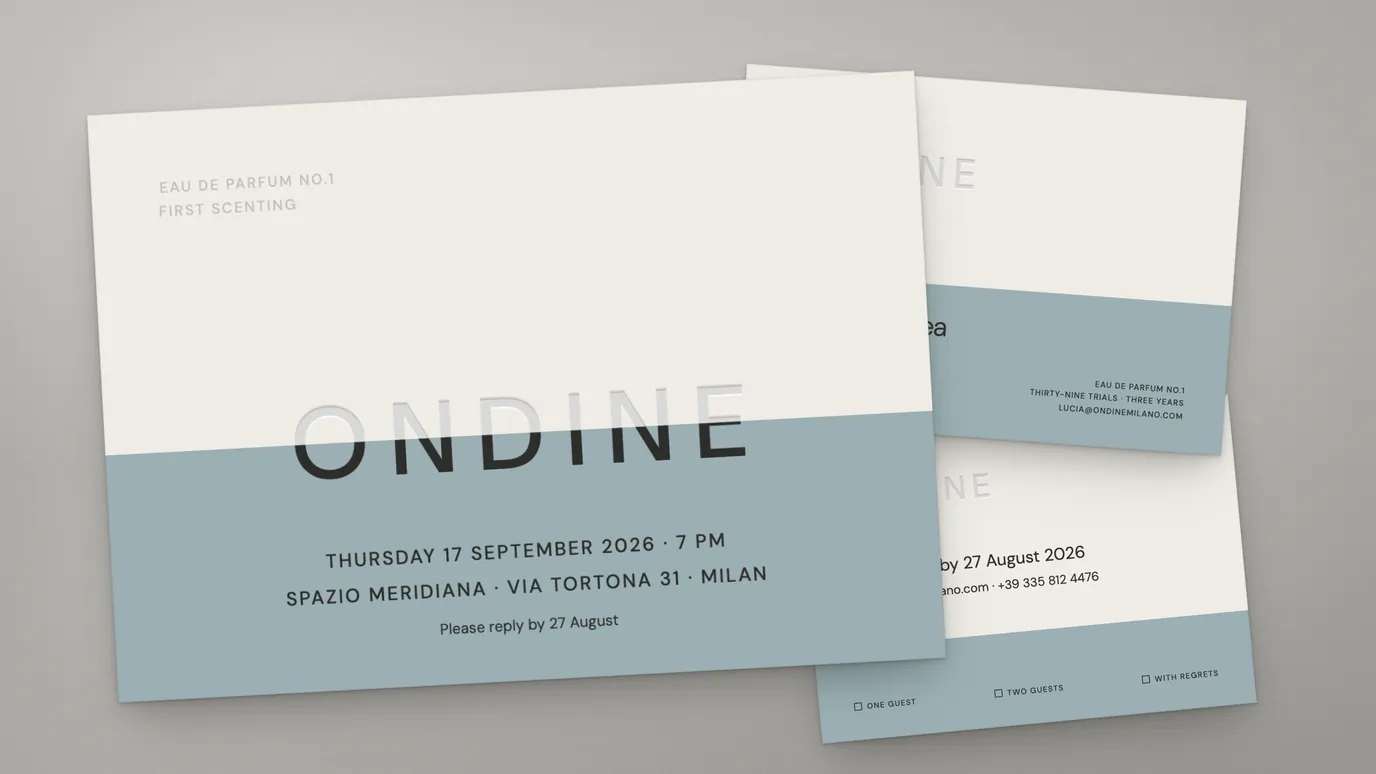 A perfume launch invitation in cream and slate blue, its wordmark pressed into the sheet without ink, beside a reply card offering one guest, two guests, or with regrets.