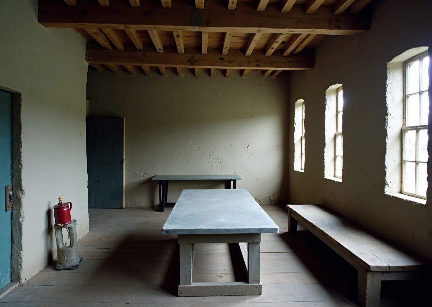 The inside of an old stone loft — lime-washed walls, bare timber joists, a plank floor, a zinc-topped table and a plain bench, lit by small deep-set windows